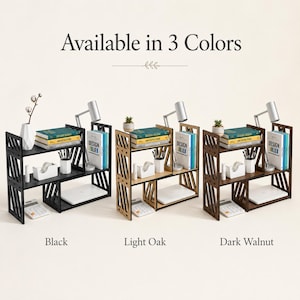 May include: Three wooden desktop organisers with a tiered, open-shelf design featuring diagonal side slats. The units are shown in black, light oak, and dark walnut finishes, each holding books, a small lamp, a plant, and office supplies.