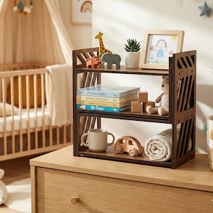 May include: A two-tier dark wood bookshelf with diagonal side slats. The top shelf holds a giraffe figurine, elephant figurine, small potted succulent, and a picture frame. The bottom shelf holds four children's books, wooden blocks, a mug, and a toy car.