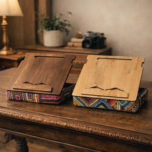 Puede incluir: Dos atriles de madera con bases bordadas de colores sobre una mesa de madera. Uno es marr&oacute;n oscuro, el otro marr&oacute;n claro. Los atriles tienen una ranura para sujetar un libro abierto.