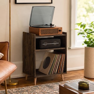 May include: A dark brown wooden record player stand with three tiers. The top tier holds a walnut-finished turntable with a clear dust cover. The middle tier contains a black rectangular speaker. The bottom tier stores a collection of vinyl records.