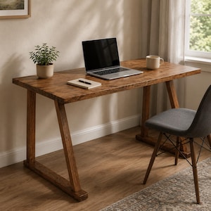 May include: A rectangular wooden desk with angled legs, featuring a laptop, a small notebook with a pen, and a potted green plant on the surface. A grey upholstered chair with wooden legs is positioned next to the desk, and a mug sits nearby.