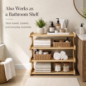 May include: A four-tier light wood shelving unit featuring text that reads: Also Works as a Bathroom Shelf. Store towels, baskets, and everyday essentials. The shelves hold folded white towels, woven baskets, glass jars, and various bathroom toiletries.