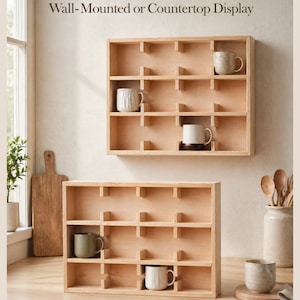 May include: Two light-colored wooden display shelves with multiple square compartments, designed for wall mounting or countertop use. The shelves feature various ceramic mugs placed inside the cubbies, showcasing a natural wood grain finish.