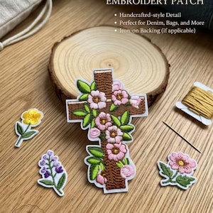 Puede incluir: Un parche de bordado de cruz floral vintage con flores rosas y hojas verdes. El parche es marrón con un borde blanco. También son visibles pequeños parches florales adicionales y una bobina de hilo dorado. El texto "VINTAGE FLORAL CROSS EMBROIDERY PATCH" está en la parte superior.