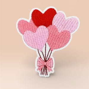 May include: Embroidered patch depicting a bunch of heart-shaped balloons in red and pink hues. The balloons are tied to a bow with a white outline, ideal for personalising garments or accessories with a romantic theme.