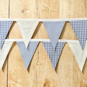 May include: A double-row fabric bunting banner featuring triangular pennants in alternating patterns of blue and white gingham, blue and white vertical stripes, and solid white. The pennants are attached to a white fabric header tape.