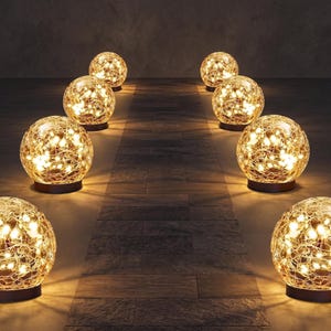 May include: A row of illuminated decorative sphere lights. Each sphere is made of a woven material, with warm white lights inside. The lights are on dark brown bases, arranged on a wooden floor.