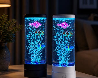 May include: Two cylindrical bubble lamps with a black and white base. The lamps feature blue bubbles and floating, colorful fish. The lamps are illuminated with blue light, creating a calming ambiance. The lamps are on a light-colored surface.