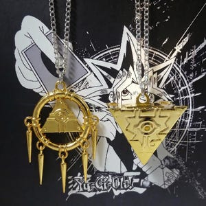 May include: Two gold-colored pendant necklaces. One is a triangle within a circle with dangling spikes, the other is a gold triangle. Both hang from silver chains. The background is black with white graphic designs and Japanese text.