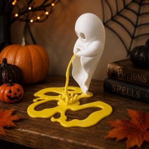 May include: A white ghost figurine standing upright, appearing to pour a stream of bright yellow liquid onto a flat, puddle-shaped yellow base. The ghost has a smooth, rounded head and a draped body, with the yellow liquid creating a splash effect.