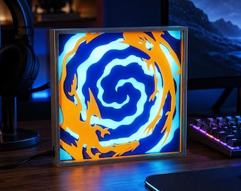 Puede incluir: Una caja de luz cuadrada e iluminada con un diseño en capas que presenta un patrón de espiral central en azul y azul claro, rodeado por siluetas naranjas con forma de dragón. El marco es de tono plateado y tiene un cable eléctrico negro.