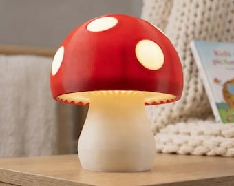 Puede incluir: Lámpara con forma de hongo con un sombrero rojo y lunares blancos. La lámpara tiene un tallo blanco y emite un brillo cálido y suave. Es una pieza decorativa, perfecta para la habitación de un niño o un espacio temático de la naturaleza.