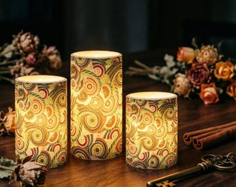 Puede incluir: Tres velas de pilar decorativas con un brillo cálido. Cada vela presenta un patrón arremolinado colorido en tonos de verde, naranja y rojo. Las velas están dispuestas sobre una superficie de madera con flores secas y palitos de canela.