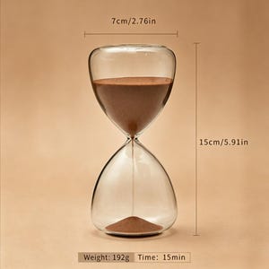 May include: Clear glass hourglass with brown sand. The hourglass is 15 inches tall and 2.76 inches wide. The weight is 192 grams, and the time is 15 minutes.