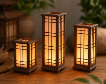 Puede incluir: Tres lámparas rectangulares con marcos de madera marrón oscuro y patrones de rejilla. Cada lámpara cuenta con paneles translúcidos que emiten un brillo naranja cálido y suave. Las lámparas varían en altura, con una unidad central alta y dos cortas.