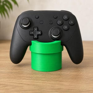 May include: A black wireless video game controller resting on a bright green cylindrical stand. The controller features a directional pad, two analogue sticks, and buttons labelled with X, Y, A, and B. The stand has a curved top cutout.