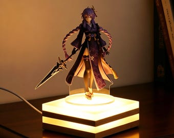 Puede incluir: Figura de un personaje con cabello púrpura y un atuendo oscuro, sosteniendo una espada. La figura se encuentra sobre una base cuadrada iluminada con un marco de madera. La base emite un brillo cálido y suave.