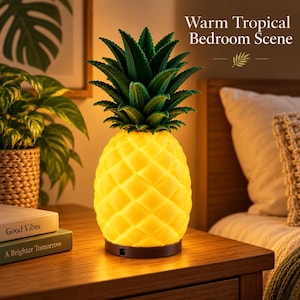 Könnte beinhalten: Eine ananasförmige Lampe mit einem leuchtend gelben Körper und strukturierten grünen Blättern an der Oberseite. Die Lampe steht auf einem dunklen runden Sockel. Der Text "Warm Tropical Bedroom Scene" ist oben rechts im Bild zu sehen.