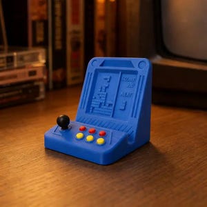 May include: A blue miniature arcade game with a black joystick and red and yellow buttons. The screen displays a Tetris game with the score and next piece visible. A retro-themed collectible.