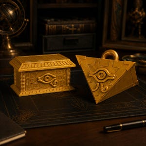 May include: A gold-colored rectangular chest and a gold-colored triangular pyramid object, both featuring the Eye of Horus symbol. The chest has engraved hieroglyphic-style markings on its side, while the pyramid has a loop at the top.