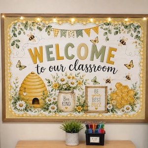 May include: A rectangular classroom bulletin board sign with a wooden frame and string lights. The sign features the text "WELCOME to our classroom" surrounded by illustrations of bees, a beehive, daisies, and a sign reading "BE YOUR BEST BUZZ".