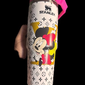 May include: White Stanley tumbler with a pink lid and handle, featuring a Minnie Mouse graphic and a repeating black and white pattern. The tumbler has the Stanley logo and a yellow and black design.
