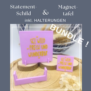以下が含まれることがあります： ピンク色のステートメントサインと、黄色で「SEI WILD FRECH UND WUNDERBAR」と書かれたマグネットボードのセット。スタンド付きで、木製の表面に表示されています。