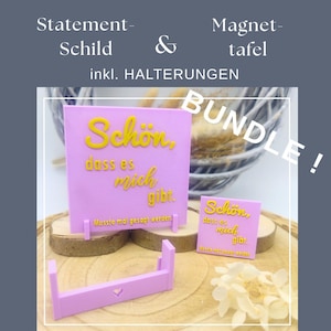 Pode incluir: Um conjunto de placas rosa e um quadro magnético com texto amarelo que diz "Schön, dass es mich gibt." O conjunto inclui um suporte e o texto "Musste mal gesagt werden." A palavra "BUNDLE" também é visível.