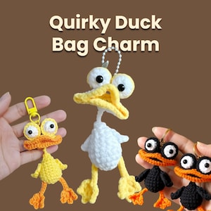 May include: Crocheted duck bag charms in yellow, orange, white, and black. The charms have large eyes and yellow beaks. The text "Quirky Duck Bag Charm" is at the top of the image. The charms are attached to keychains.