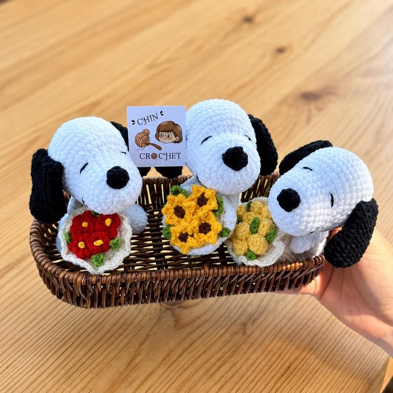 May include: Three white and black crocheted dog figures with floppy ears and black noses, each holding a small crocheted flower bouquet in red, yellow, or light yellow. A small white tag reads CHIN CROCHET with an illustration.
