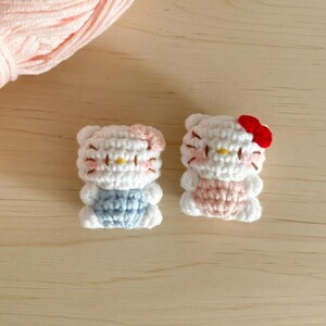 May include: Two handmade crochet figures of a popular cartoon character. One figure has a blue outfit and a pink bow, the other has a pink outfit and a red bow. The figures are white with black details and yellow noses.