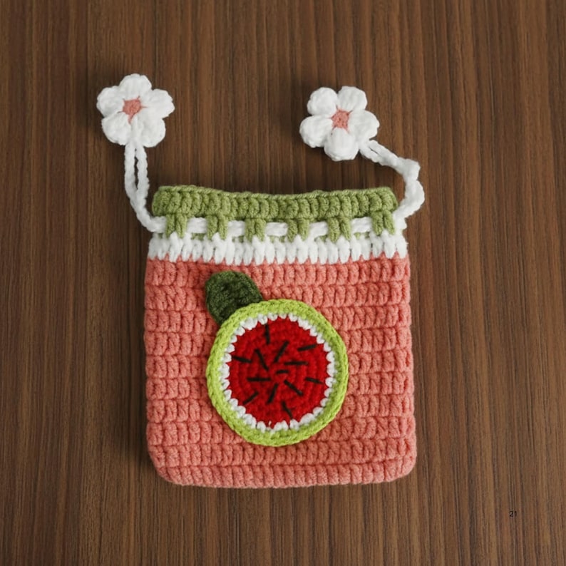 K&ouml;nnte beinhalten: Eine handgefertigte H&auml;keltasche in Hellkoralle, mit einem Wassermelonen-Applikation. Die Tasche hat eine gr&uuml;ne und wei&szlig;e Bord&uuml;re und ist mit zwei wei&szlig;en Blumen verziert. Die Tasche ist etwa 13 cm breit und 15 cm hoch.