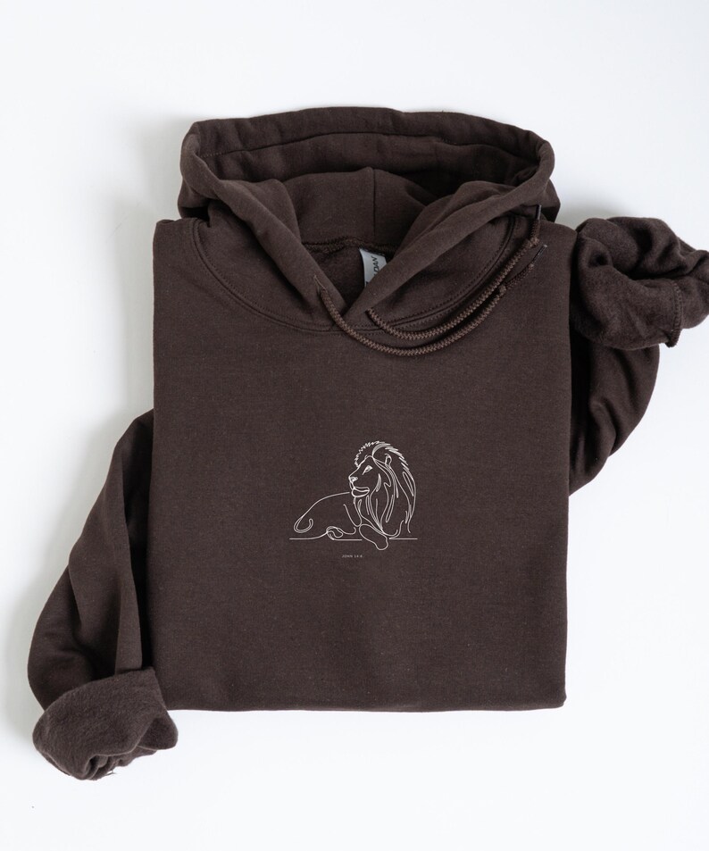 May include: A dark brown hoodie with a white line drawing of a lion on the front. The hoodie has a drawstring hood and long sleeves. The lion illustration is simple and elegant, with the words "GOOD VIBES" below it.
