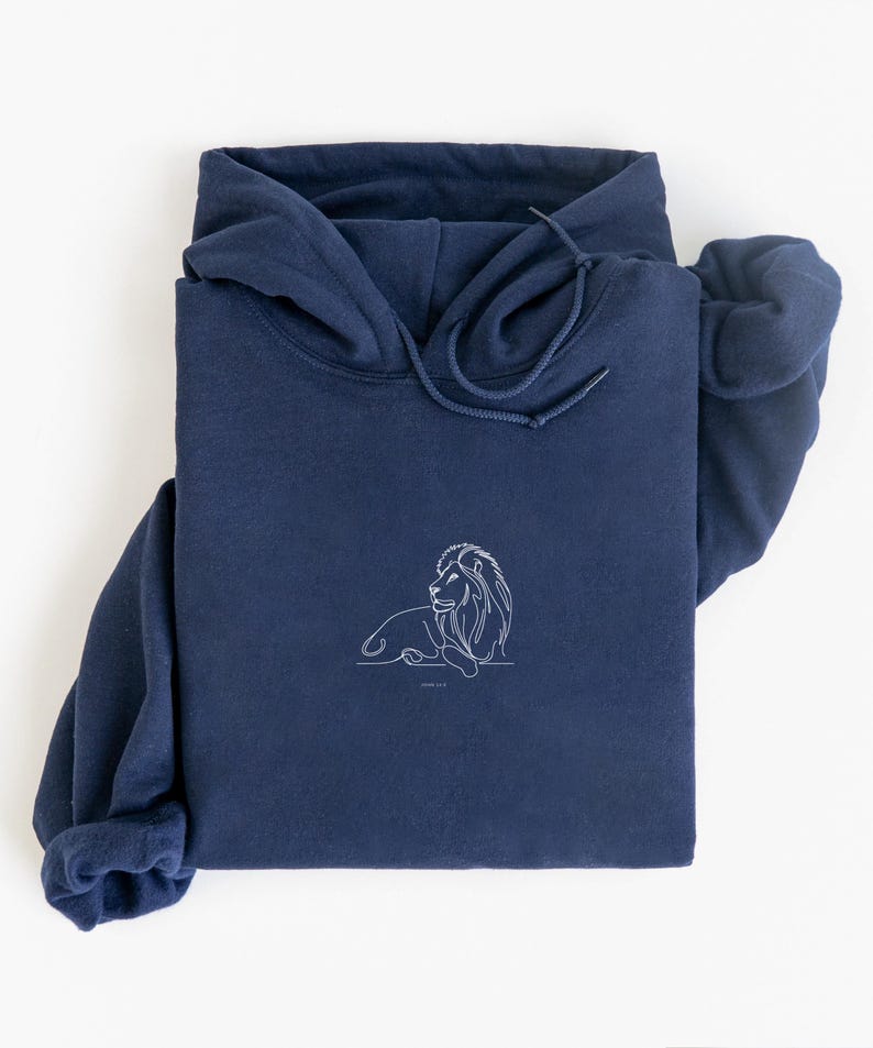 May include: A navy blue hoodie with a white line drawing of a lion on the front. The hoodie has a drawstring hood and long sleeves. The lion design is simple and elegant, with the text "JOHN 1:12" below it.