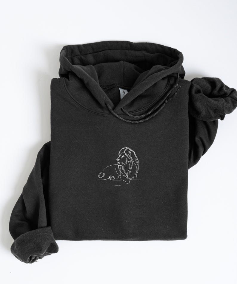 May include: A black hoodie with a white line drawing of a lion. The lion is lying down with its head turned to the side. The hoodie has a drawstring hood and long sleeves. The image is on a white background.