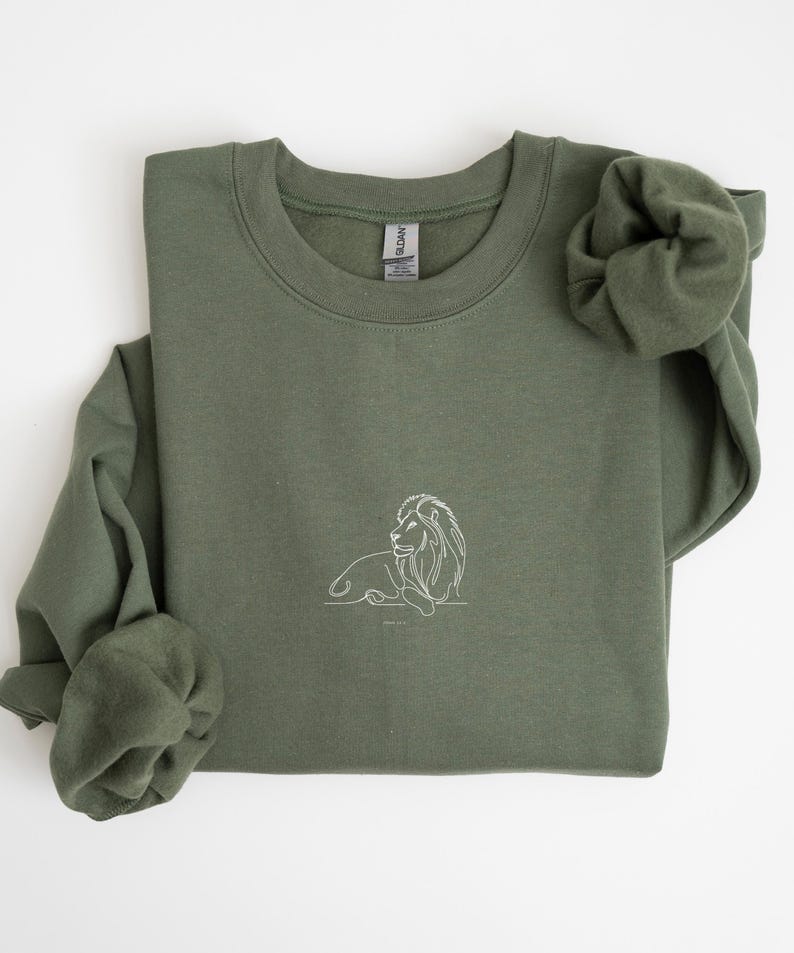 May include: Olive green sweatshirt with a white line drawing of a lion. The crew neck sweatshirt has long sleeves and a relaxed fit. The lion illustration is on the lower right side of the shirt.