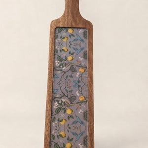 May include: A long, rectangular wooden serving board with a handle at the top. The centre features an inset panel with a grey background decorated with a repeating pattern of yellow lemons, green leaves, white flowers, and blue hummingbirds.