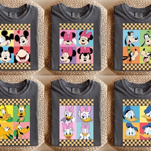 May include: Six gray t-shirts with colorful pop art designs featuring Disney characters. Each shirt has a different design, including Mickey Mouse, Minnie Mouse, Goofy, Daisy Duck, and Donald Duck, set against a checkered border.