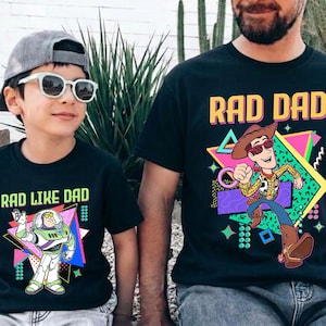 May include: Black t-shirts with matching graphics. One shirt says "RAD DAD" with a cartoon Woody character, and the other says "RAD LIKE DAD" with a Buzz Lightyear graphic. Both shirts have a retro 80s design.
