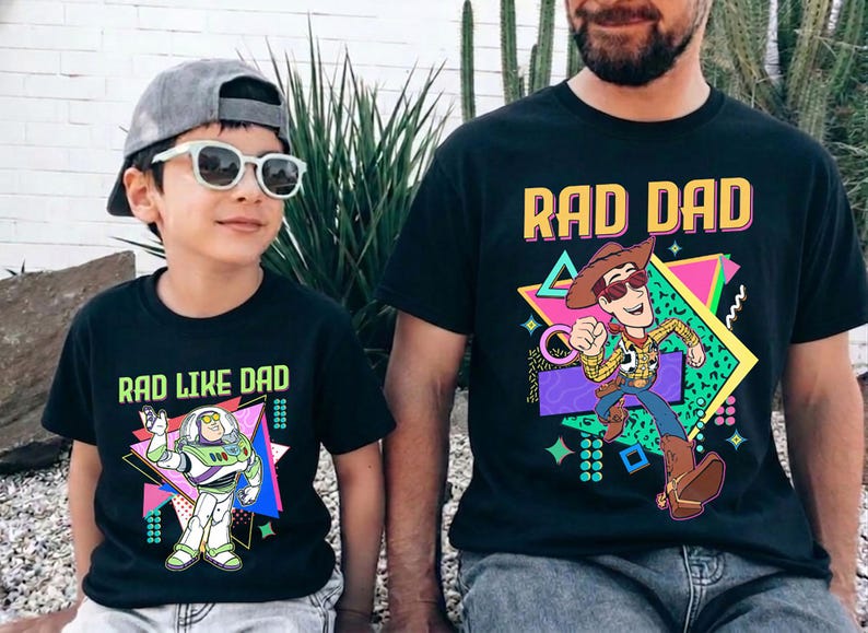 May include: Black t-shirts with matching graphics. One shirt says "RAD DAD" with a cartoon Woody character, and the other says "RAD LIKE DAD" with a Buzz Lightyear graphic. Both shirts have a retro 80s design.