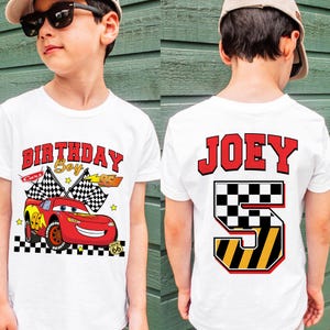 May include: White t-shirt featuring a red race car graphic with the text "BIRTHDAY Boy" and "95". The back of the shirt displays the name "JOEY" and the number "5" in a checkered and yellow design. The shirt is for a child.