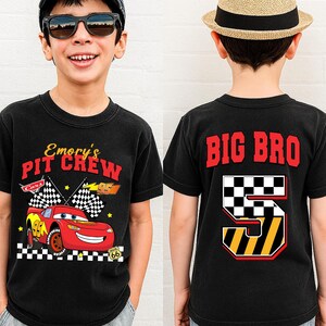 May include: Black t-shirt with a red race car graphic and the text "Emory's Pit Crew" on the front. The back of the shirt says "BIG BRO" with a number 5 design. The shirt is for a child.