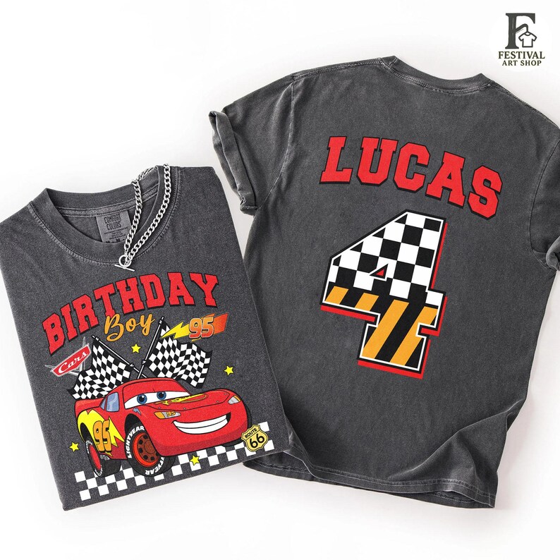 May include: Two gray t-shirts with racing car graphics. One shirt says "BIRTHDAY BOY" with a red race car and checkered flags. The other shirt has the name "LUCAS" and the number "4" with a checkered flag design.