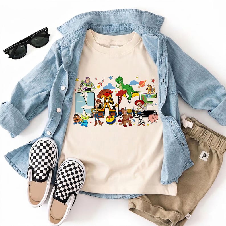 Puede incluir: Una camiseta color crema con la palabra "NAME" en un dise&ntilde;o colorido con personajes de la pel&iacute;cula Toy Story. La camiseta se combina con una camisa vaquera azul claro, pantalones cortos color caqui y zapatos sin cordones a cuadros blancos y negros. Tambi&eacute;n se incluyen gafas de sol.