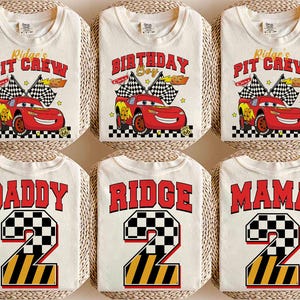 May include: Cream-colored t-shirts with various designs. Some shirts feature a red race car with the text "Ridge's Pit Crew" and "Birthday Boy". Other shirts display "Daddy", "Ridge", and "Mama" with a number 2 in a checkered and striped design.