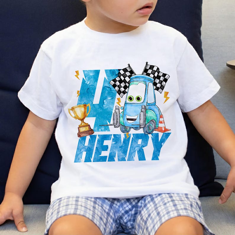 May include: White t-shirt with a blue and green cartoon car graphic, checkered flags, and a gold trophy. The number "4" and the name "HENRY" are printed in blue. A fun birthday shirt for a child.