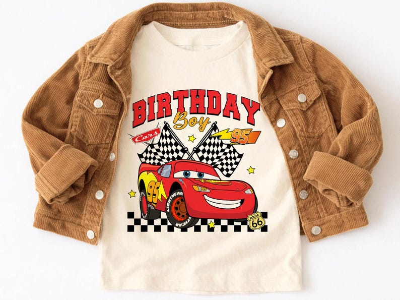 May include: A tan t-shirt featuring a red race car graphic with the text "BIRTHDAY Boy" and the number "95". The shirt is layered under a brown corduroy jacket.