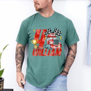 May include: Teal green t-shirt featuring a watercolor illustration of a red cartoon truck with checkered flags and a gold trophy. The number 4 and the name "WILLIAM" are printed in red.