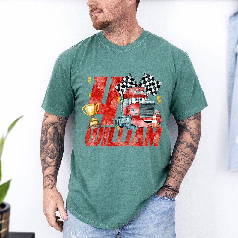 May include: Teal green t-shirt featuring a watercolor illustration of a red cartoon truck with checkered flags and a gold trophy. The number 4 and the name "WILLIAM" are printed in red.