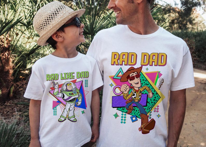 May include: White t-shirts with cartoon graphics. One shirt says "RAD DAD" with a Woody character, the other says "RAD LIKE DAD" with a Buzz Lightyear character. Both shirts have colorful geometric designs.